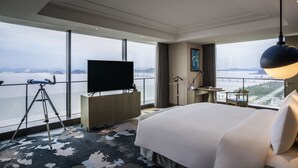 A hotel room with a large bed, a desk with a flat-screen TV, a telescope, and a view of a body of water and cityscape. - Pullman Zhoushan Seaside (Zhoushan)
