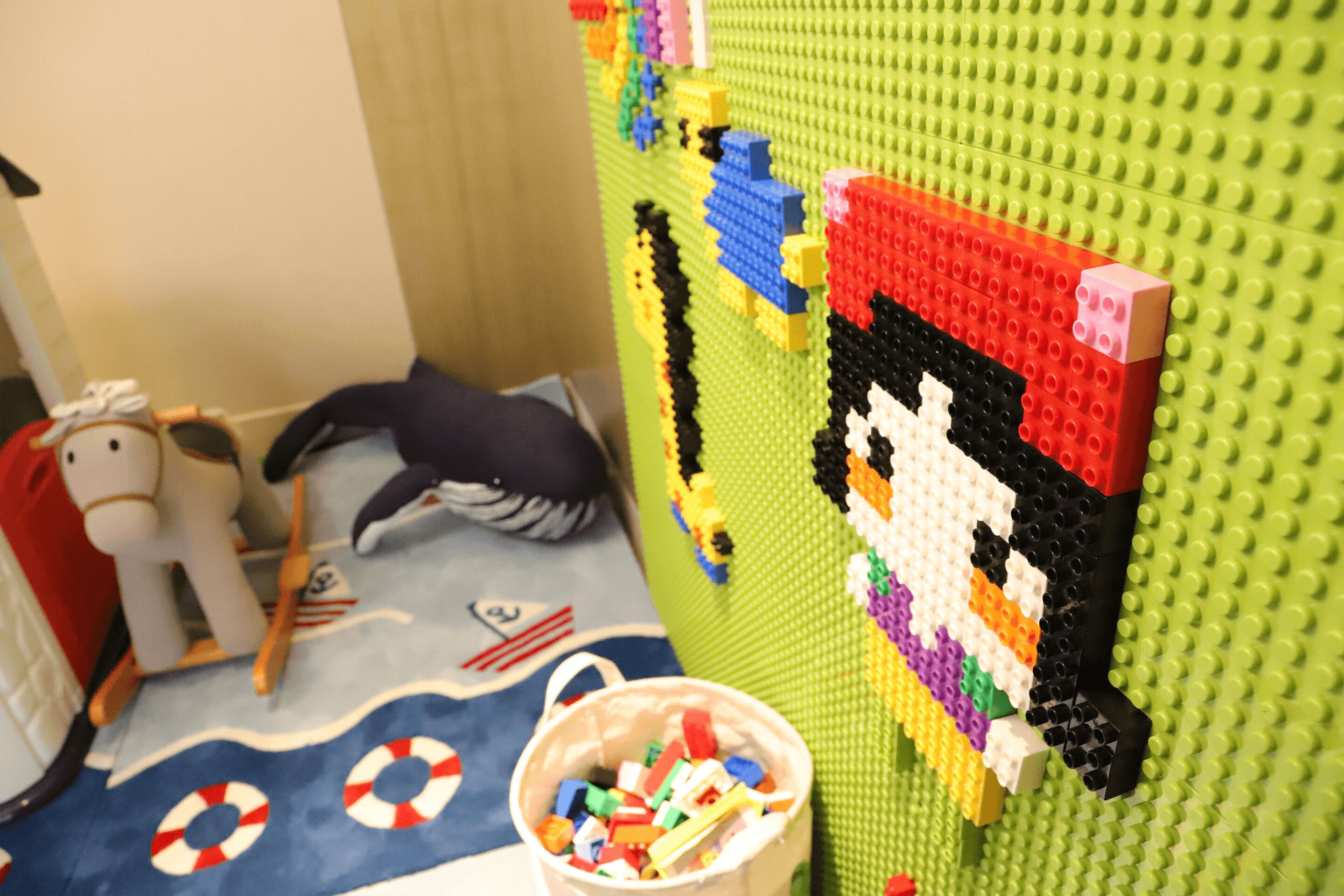 A LEGO wall with a pixelated character, a bucket of LEGO pieces, and a toy horse.
