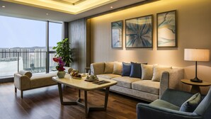 A modern living room with a sofa, armchairs, a coffee table, and a lamp. There are large windows offering a view of buildings outside. - Pullman Zhoushan Seaside (Zhoushan)
