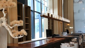 A modern reception area with a wooden reception desk, a large window, and a decorative tree sculpture. - Novotel Deqing Moganshan (Huzhou)