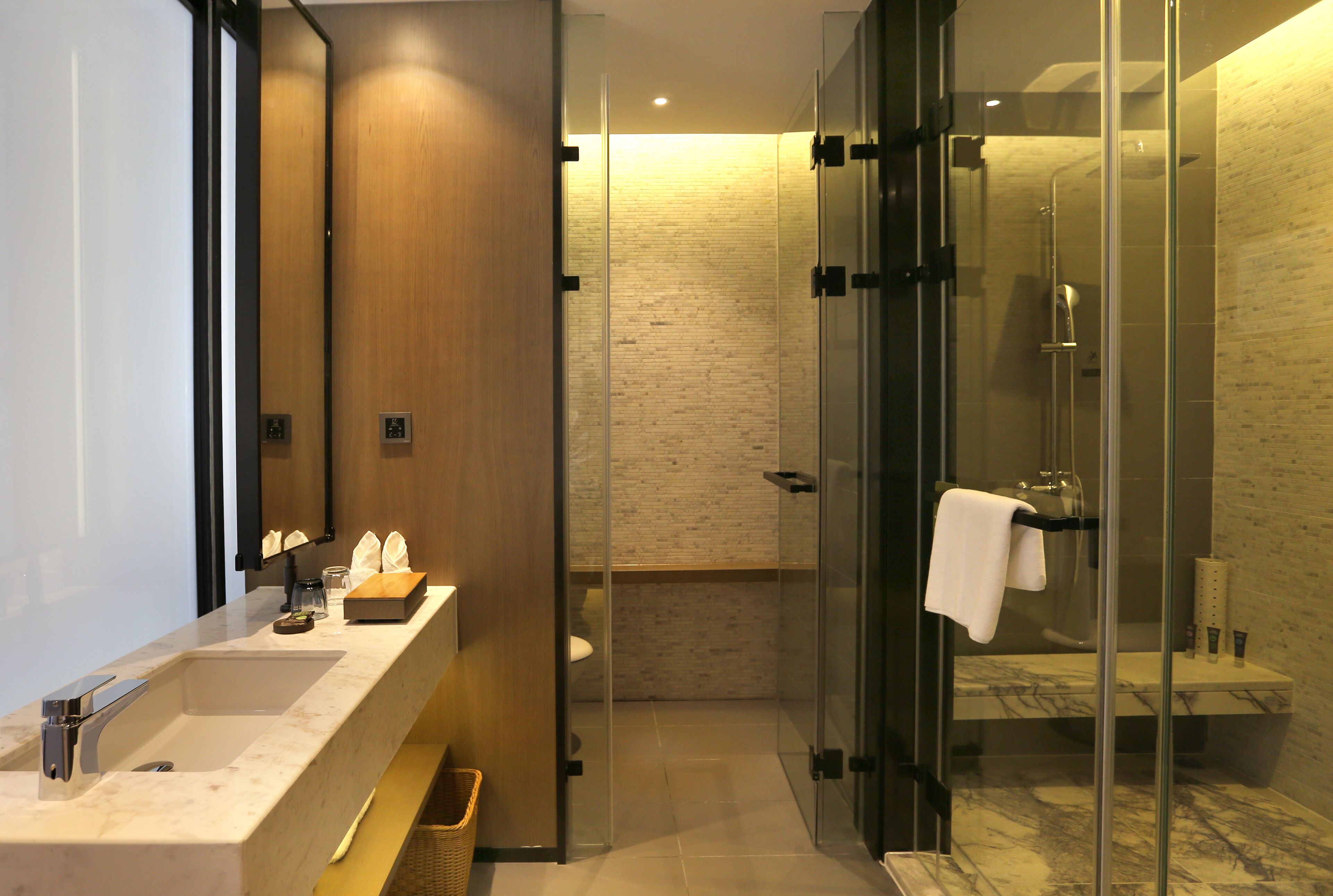 A modern bathroom with a glass-enclosed shower, a wooden vanity, and a marble sink.