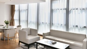A modern living room with a sofa, armchairs, a coffee table, and a dining area with a table and chairs. - Novotel Deqing Moganshan (Huzhou)