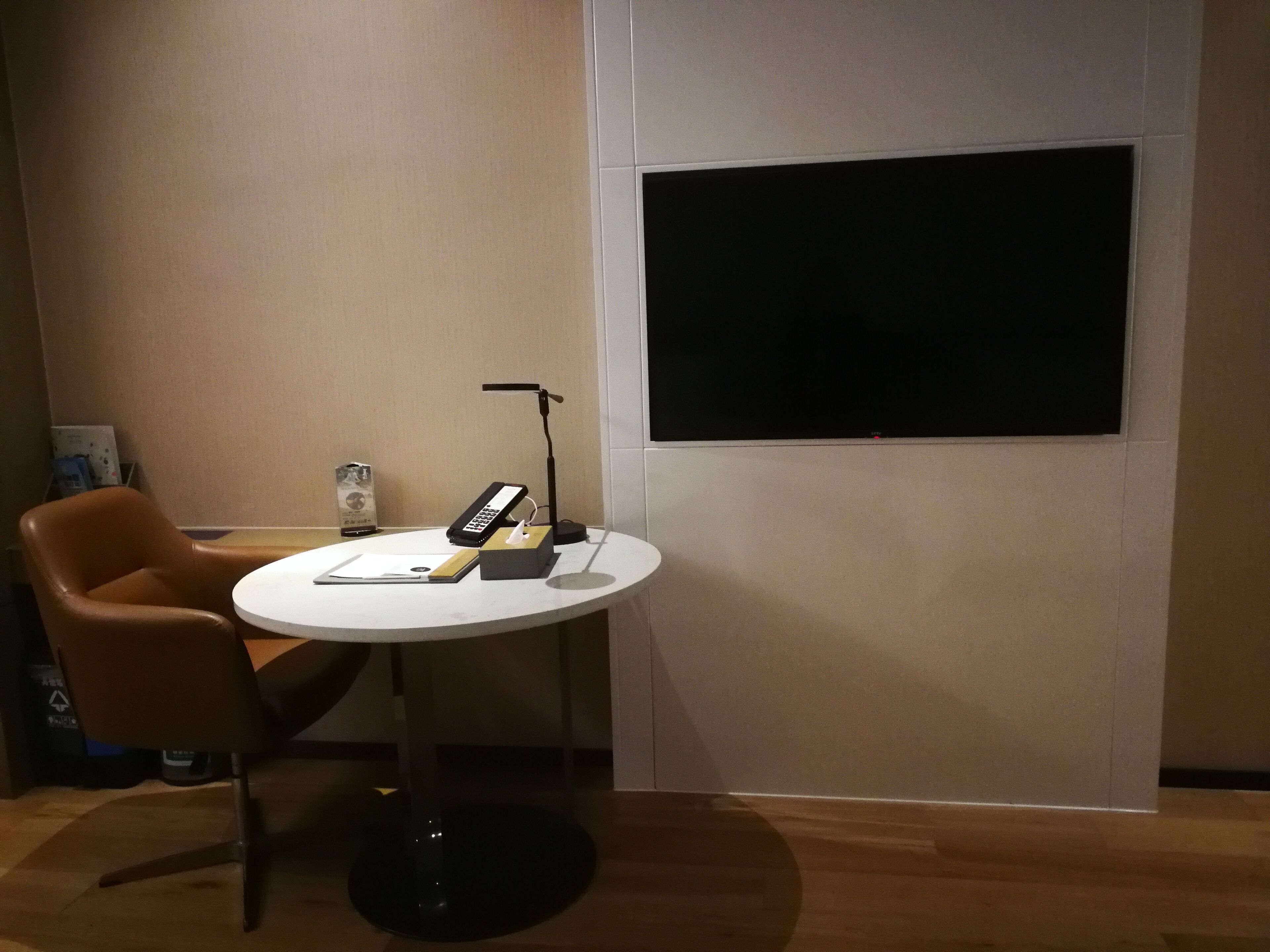 Une salle de conférence avec une table blanche, un fauteuil en cuir marron, un pied de micro noir et un grand écran noir fixé au mur.