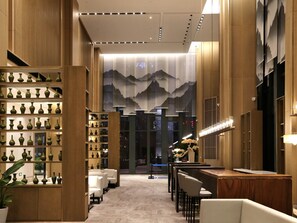 A modern interior with a central corridor, wooden shelving with vases, seating areas, and a decorative wall with mountain imagery. - Novotel Deqing Moganshan (Huzhou)