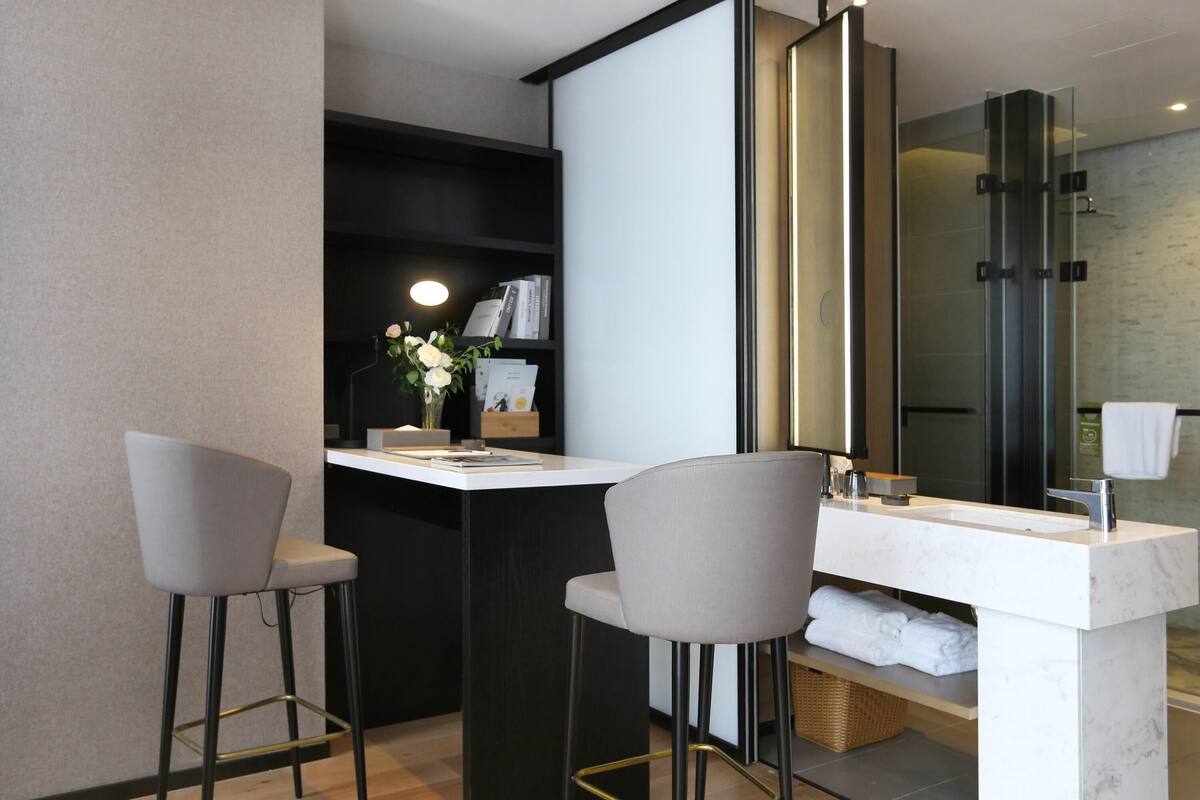A modern bathroom with a white vanity, two grey bar stools, a large mirror, and a glass shower enclosure.
