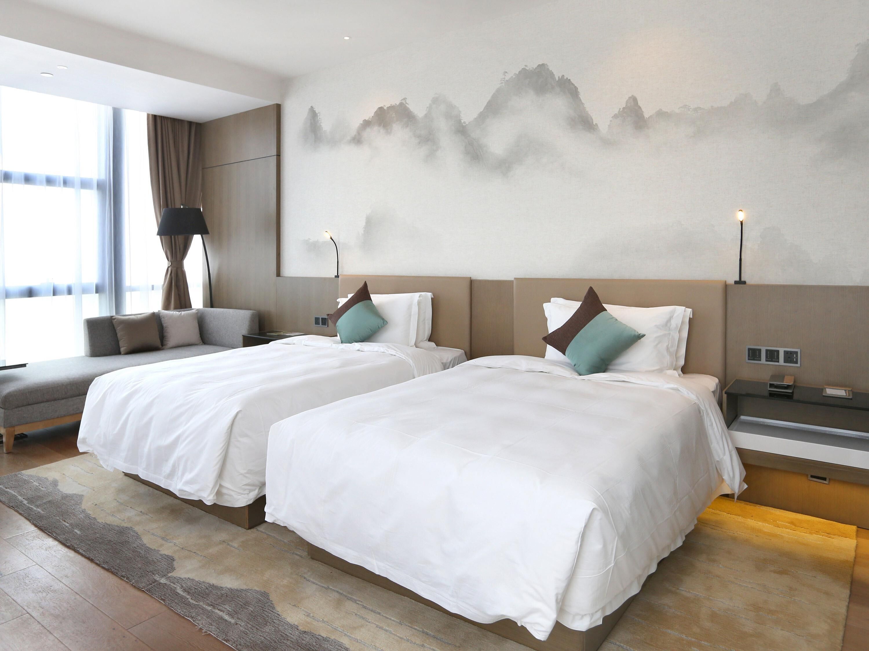 Habitación de hotel con dos camas, un sofá y un mural grande en la pared.