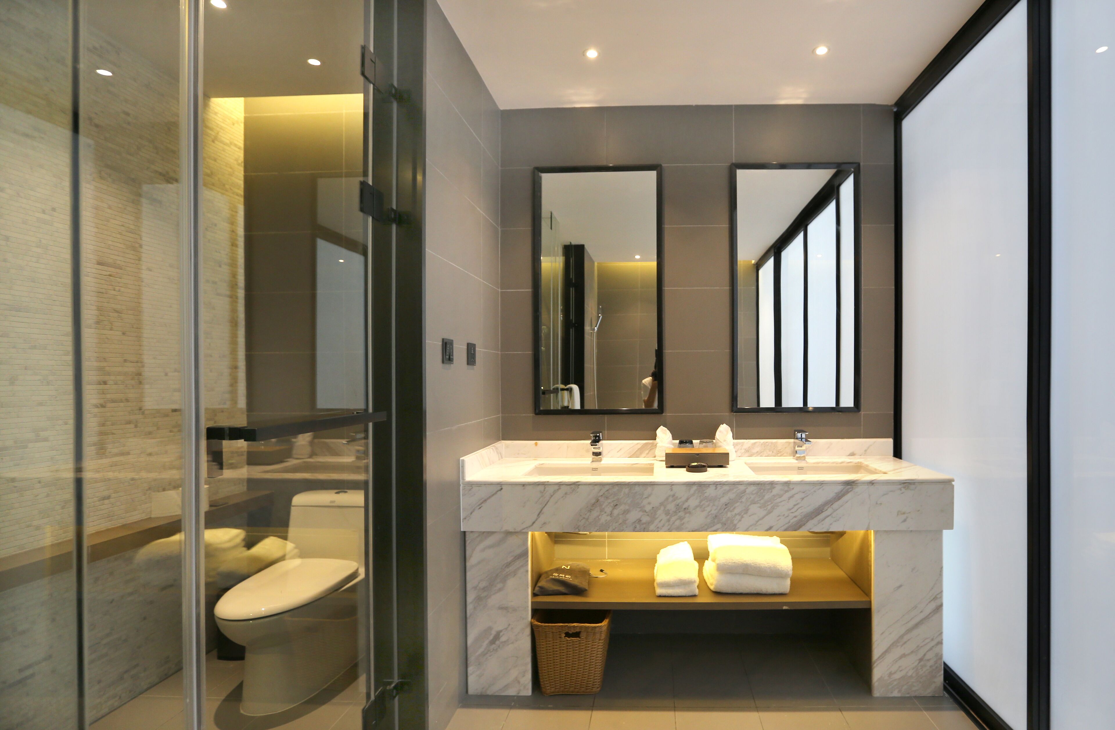 Un baño moderno con ducha envuelta en vidrio, lavabo de mármol y un espejo grande.