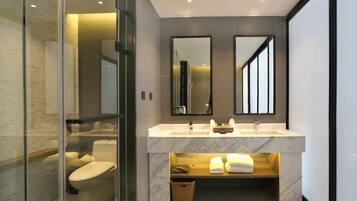 Un baño moderno con ducha envuelta en vidrio, lavabo de mármol y un espejo grande.