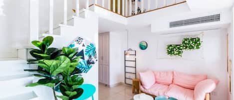 A modern living room with a staircase, a pink sofa, a coffee table, and a large plant.