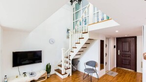 Un salon moderne avec un plancher en bois, un téléviseur à écran plat, un canapé blanc, un escalier doté de rampes en verre et une porte en bois foncé.