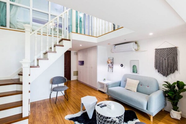 A spacious living area with a staircase, a light blue sofa, a small round table, and a potted plant. - LIVE INN Chuansha (Shanghai)