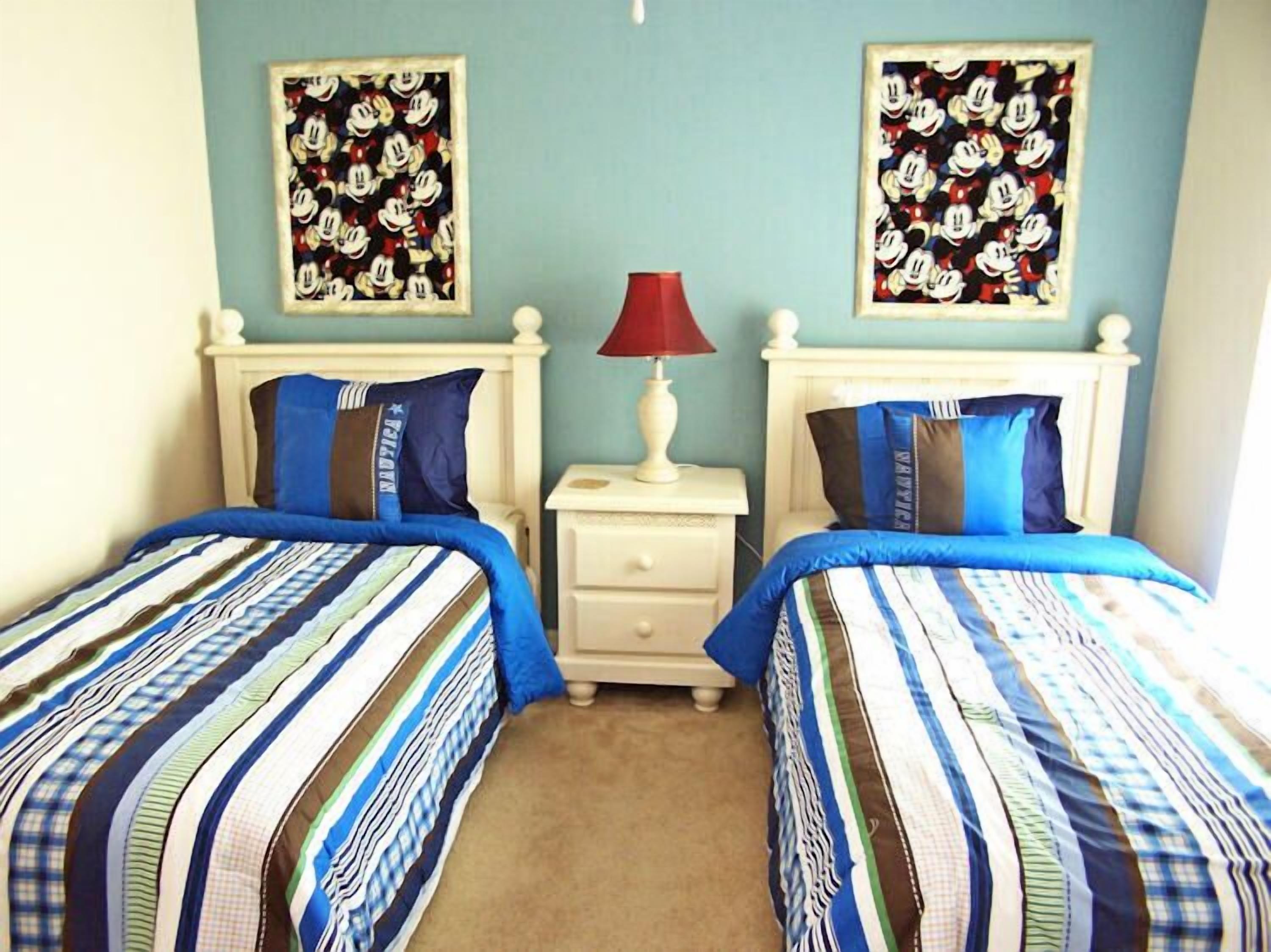 A bedroom with two beds, each with striped bedding, a nightstand with a lamp, and two framed pictures on the wall.