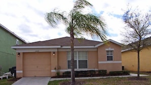 A single-story house with a garage, a small front yard with grass and a palm tree, and a clear sky. - Fs54755 - Sandy Ridge - 4 Bed 3 Baths Villa (Davenport)