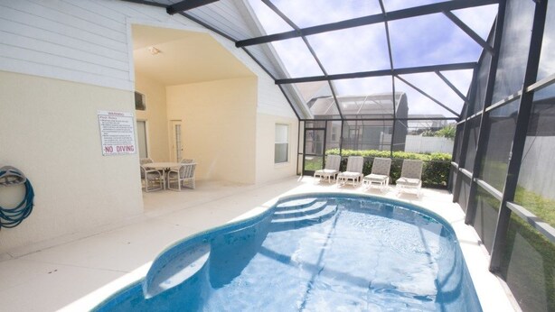Una piscina interior con techo de cristal, rodeada de sillones de descanso y un cartel que indica prohibido bucear.