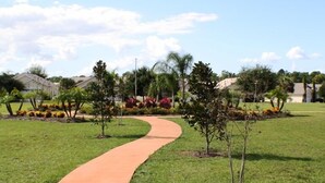 Un camino curvo en un área verde bien cuidada, con árboles pequeños y macizos de flores.
