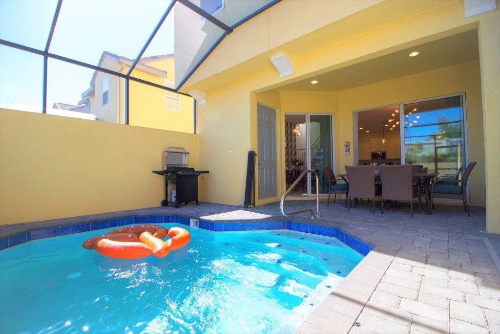 Une piscine avec un jacuzzi, un espace barbecue et un coin repas avec des sièges extérieurs.