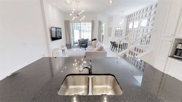 A modern kitchen with a double sink, a dining area with a sofa, and a staircase leading to an upper level. - Aco248528 - Festival Resort - 5 Bed 5.5 Baths Townhome (Davenport)