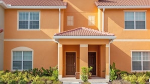 A two-story building with a red-tiled roof, a central entrance with a door, and a small porch area. - Fv50095 - Paradise Palms - 4 Bed 3 Baths Townhome (Kissimmee)