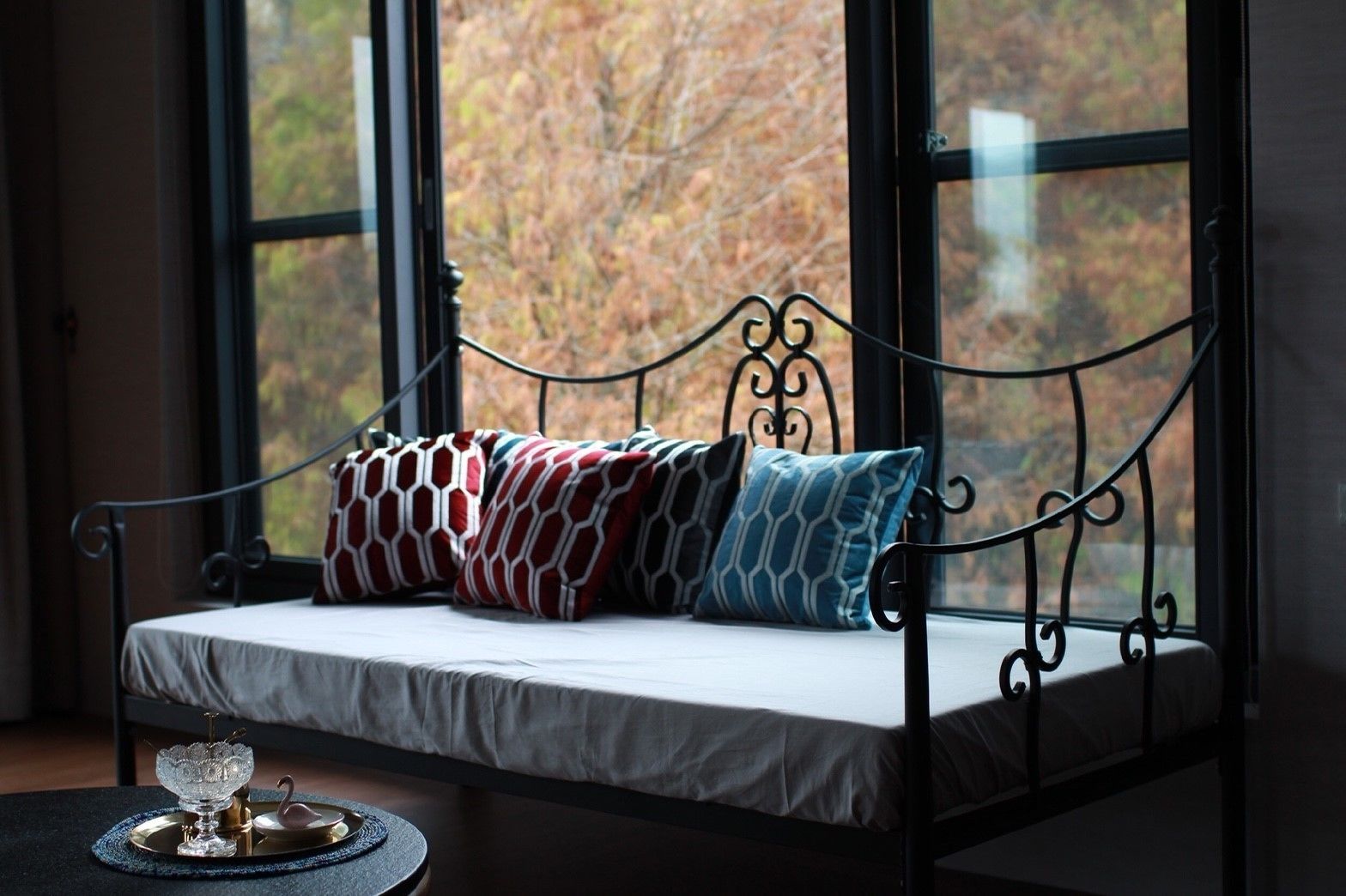 A wrought iron bench with a cushioned seat and backrest, adorned with patterned cushions.