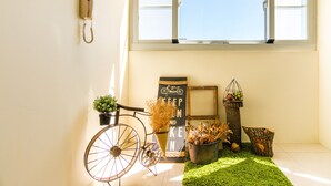 A room with a bicycle, a wall-mounted phone, a sign with a bicycle and text, a planter with dried flowers, and a small table with a candle and a birdcage. - Cozy Green Guest House (Taitung)