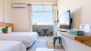 A hotel room with two beds, a desk with a computer, a TV, and a balcony with a view. - Cozy Green Guest House (Taitung)