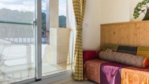 A room with a bed, a wooden headboard, a window with curtains, and a view of a balcony and mountains. - Cozy Green Guest House (Taitung)