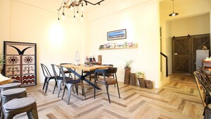 A dining area with a wooden herringbone floor, a round table with chairs, and a hanging light fixture. - Cozy Green Guest House (Taitung)