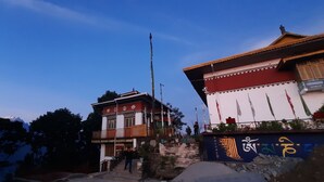A traditional building with a sign reading "Uddise Monks Cooperative Shop" and a flagpole with flags. - Mochilero Ostello (Gyalshing)