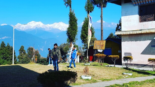 A building with a signboard, a flag, and a view of snow-capped mountains in the background. - Mochilero Ostello (Gyalshing)