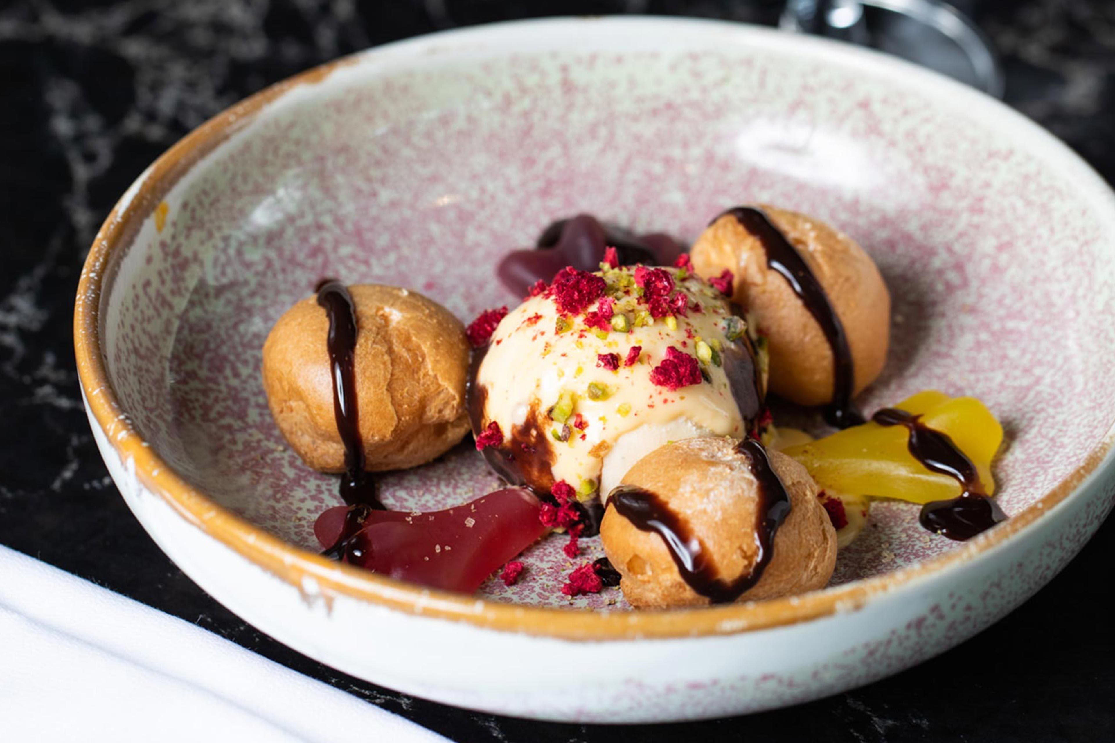 Une assiette de dessert avec trois pâtisseries rondes, une boule de glace et un filet de chocolat.