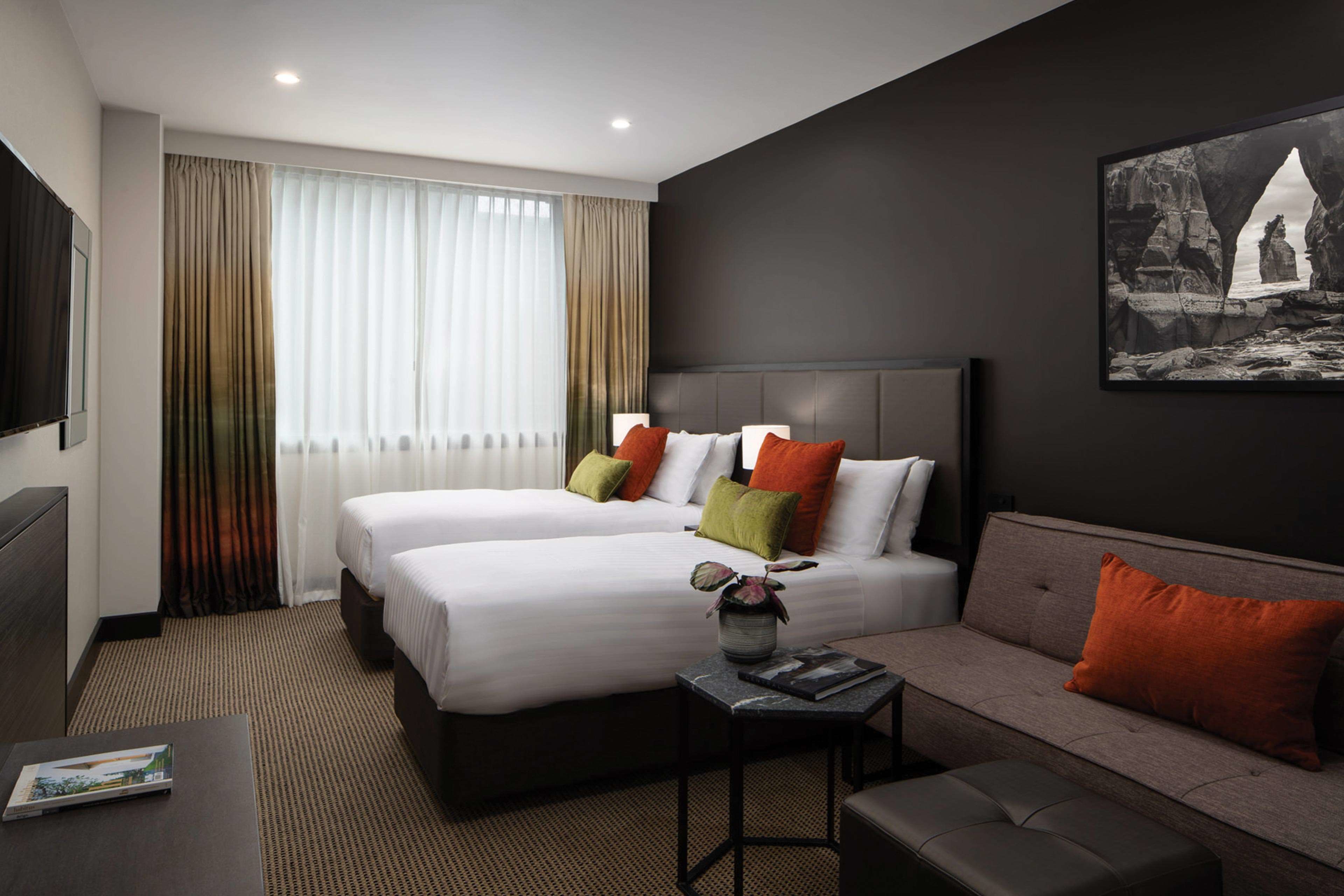 A hotel room with two beds, a sofa, a small table, and a TV.