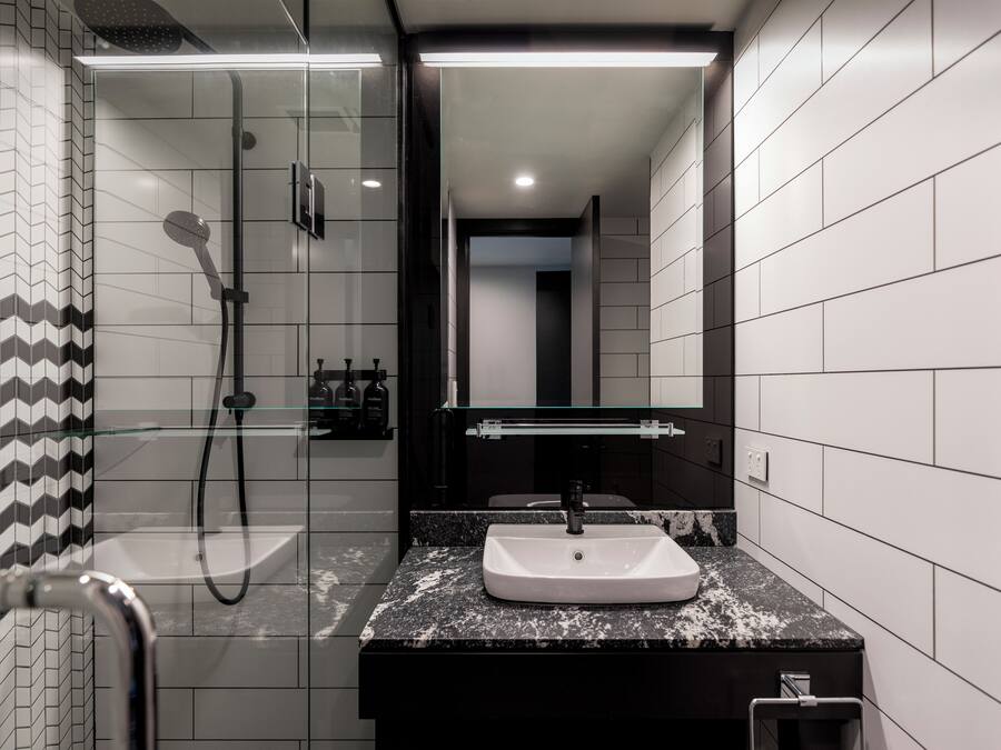 Ein modernes Badezimmer mit einer gläsernen Duschkabine, einem weißen Waschbecken und einer schwarzen Arbeitsplatte.