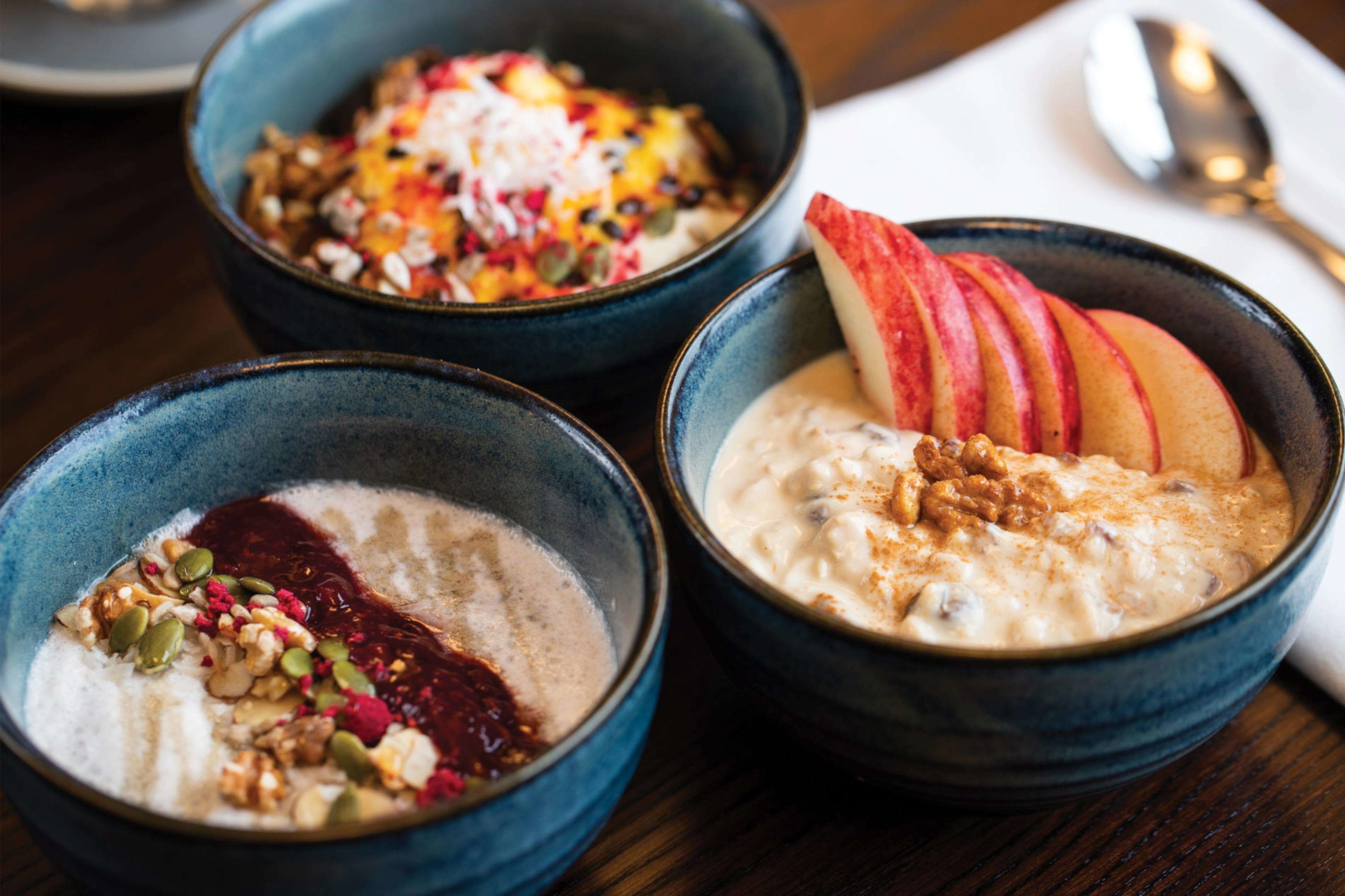 Three bowls of oatmeal with toppings on a wooden table.