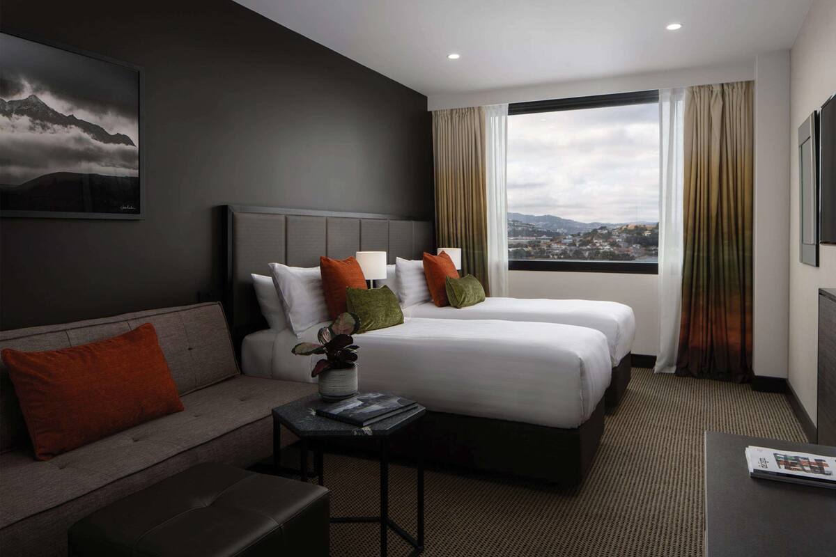 A hotel room with two beds, a sofa, a small table, and a view of the city.