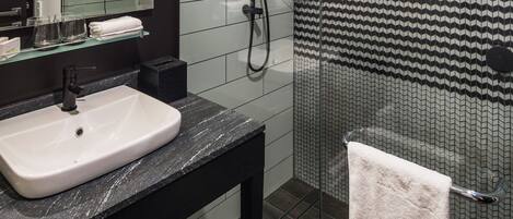 Un baño moderno con un lavamanos blanco, encimera negra y cabina de ducha de vidrio.
