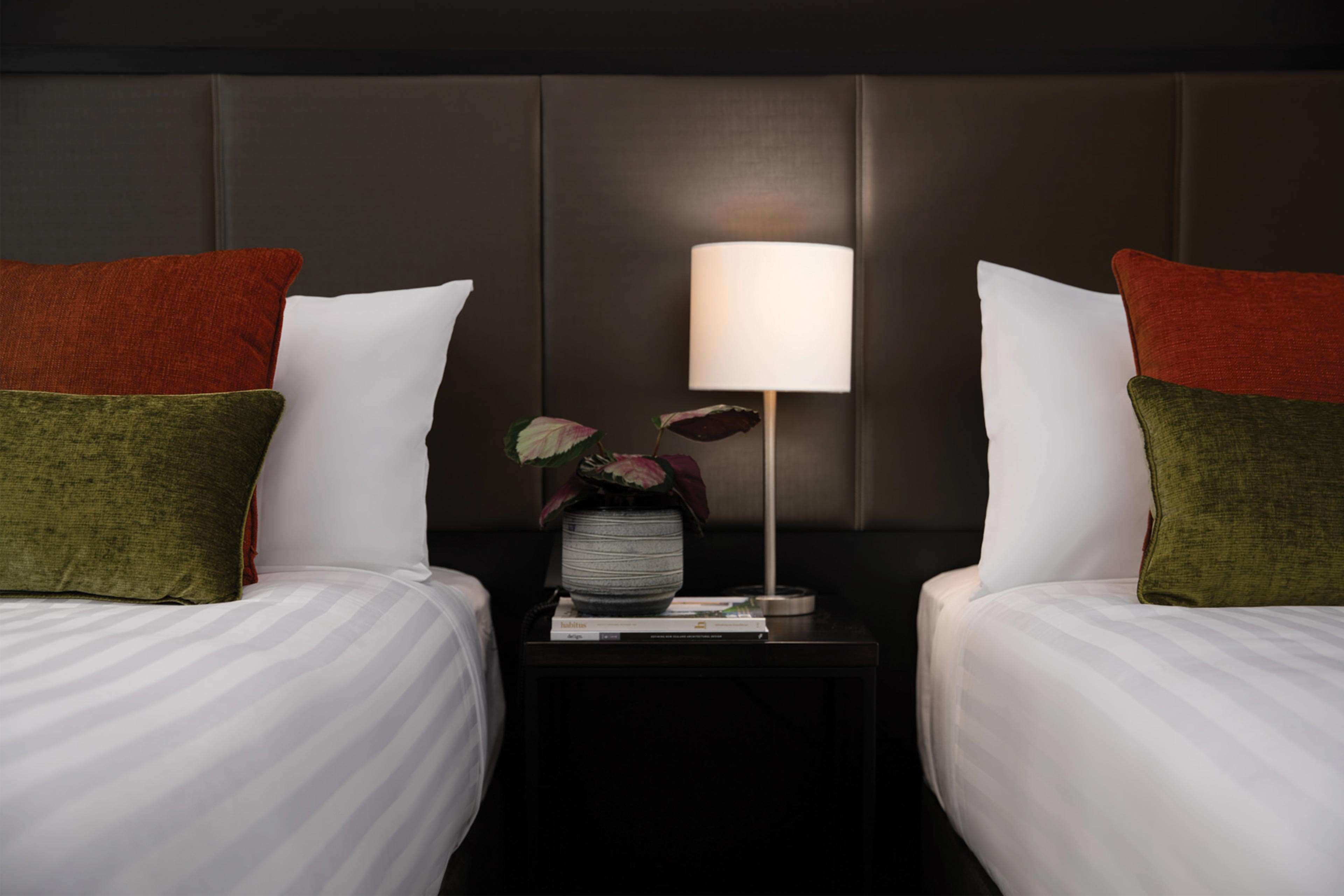 A hotel room with two beds, a nightstand with a lamp, and a vase with flowers.