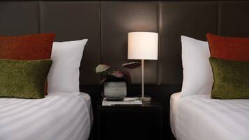 A hotel room with two beds, a nightstand with a lamp, and a vase with flowers.