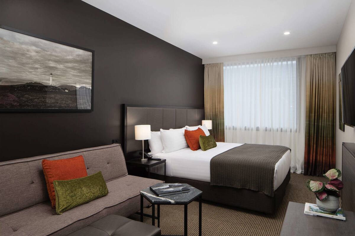 A modern hotel room with a large bed, a sofa, a small table, and a painting on the wall.