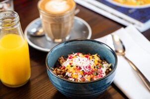 Impostazione colazione con una ciotola di cereali guarnita con frutta e noci, un bicchiere di succo d'arancia e una tazza di caffè su un tavolo.