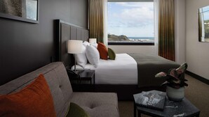 A hotel room with a bed, a sofa, a small table with a book and a plant, and a window with curtains. - Rydges Wellington Airport (Wellington)
