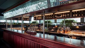 A bar area with a wooden counter, shelves of bottles, and a martini glass. - Rydges Wellington Airport (Wellington)