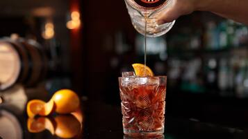 A bar setting with a glass of amber-colored drink garnished with an orange slice, ice cubes, and a bar tool.