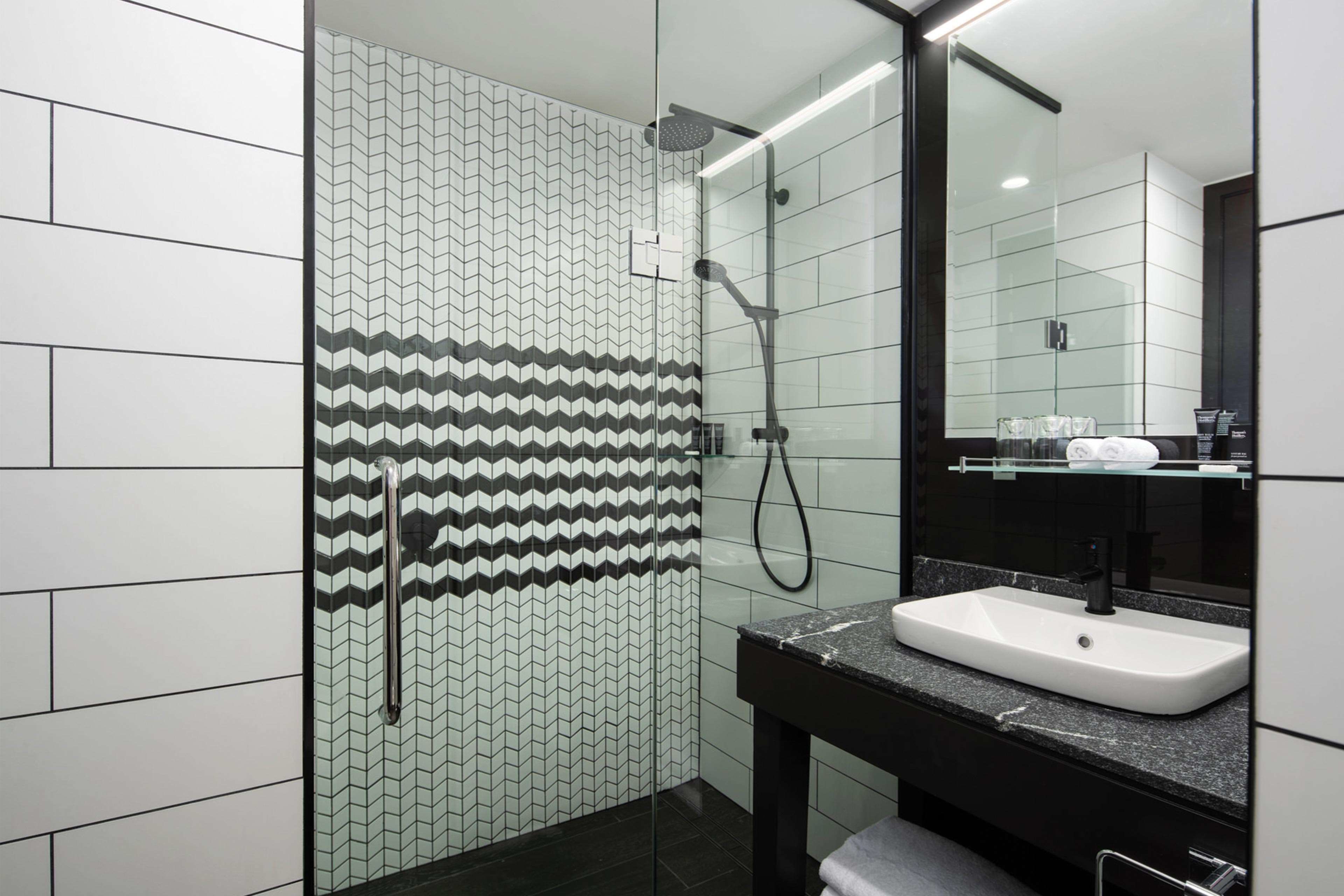 A modern bathroom with a glass-enclosed shower, a white sink with a black countertop, and a mirror above the sink.