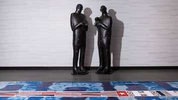 Zwei schwarze Statuen auf einem gemusterten Teppich vor einer schlichten Wand.