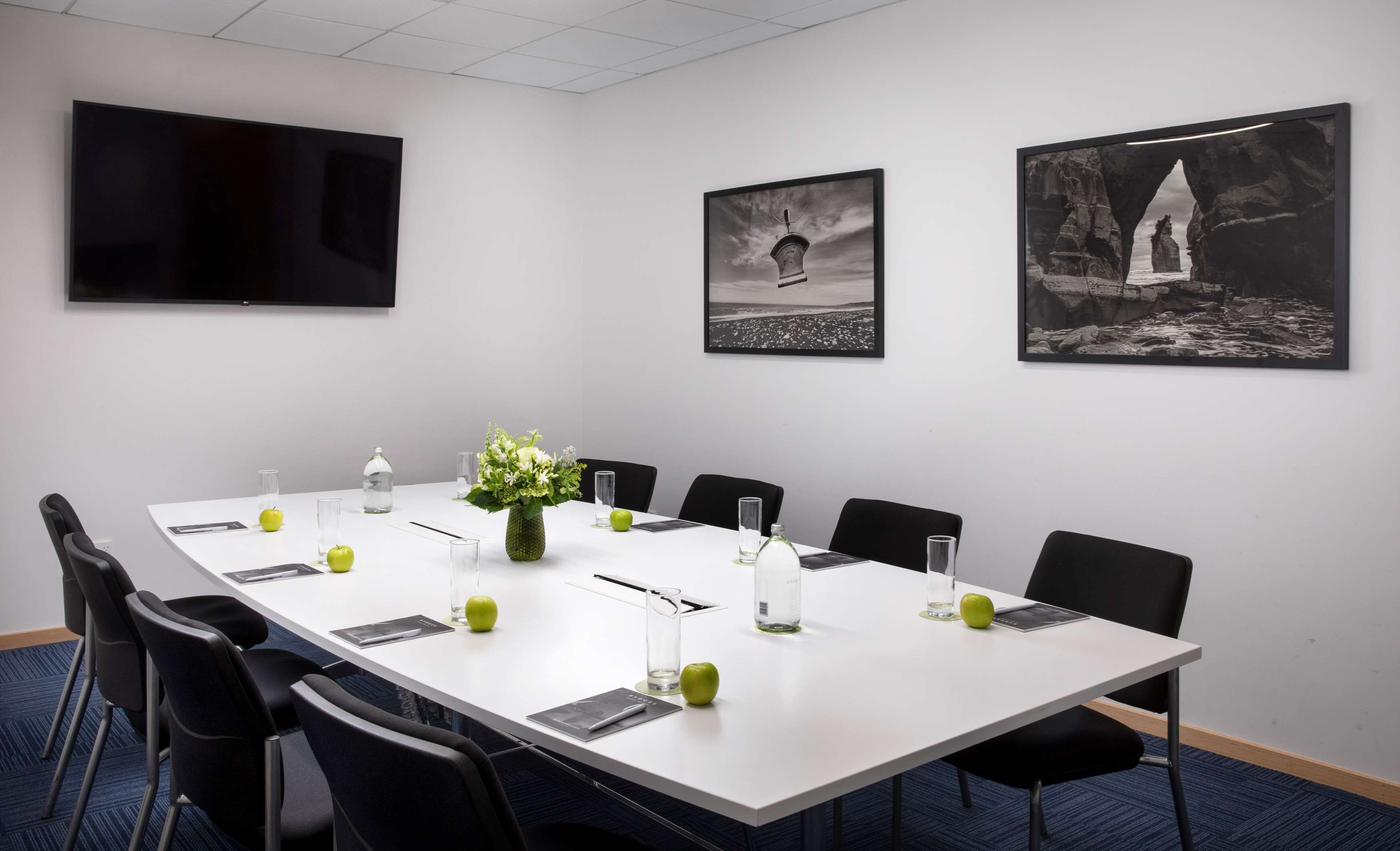 Una sala conferenze con un lungo tavolo, sedie, un televisore e quadri appesi al muro.