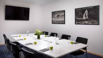 Ein Konferenzraum mit langem Tisch, Stühlen, einem Fernseher und gerahmten Bildern an der Wand.