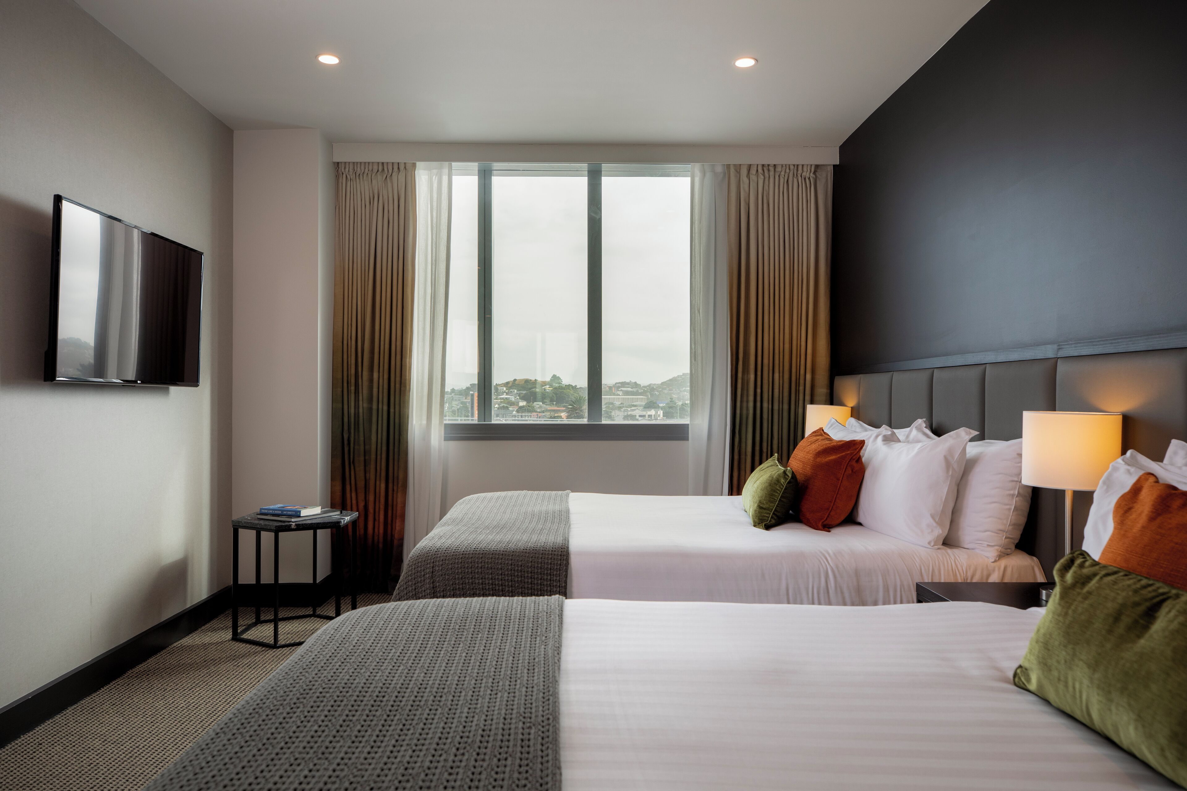 Habitación de hotel con dos camas, televisor, ventana con cortinas y vista a la ciudad.