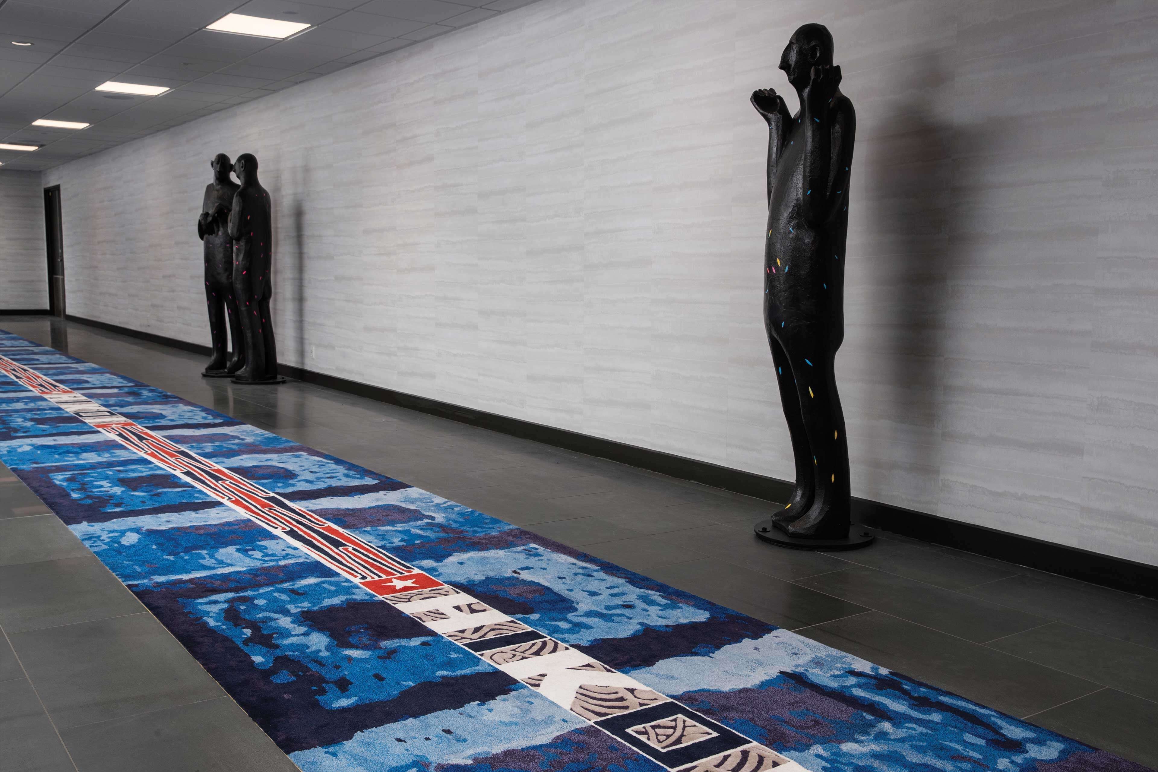 A hallway with a patterned carpet, three black statues, and a white brick wall.