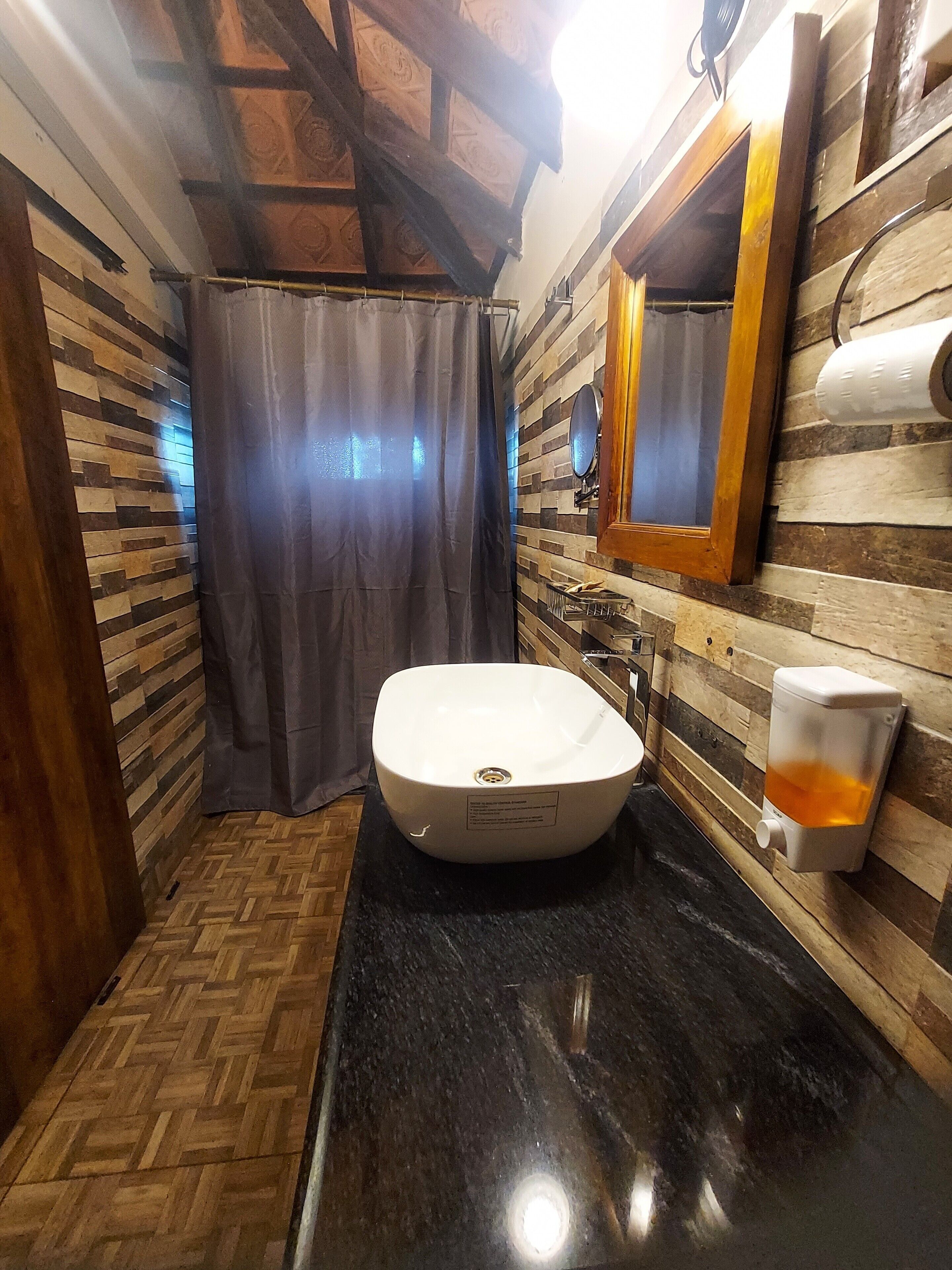 A bathroom with a wooden herringbone floor, a white sink, a mirror, and a towel dispenser.