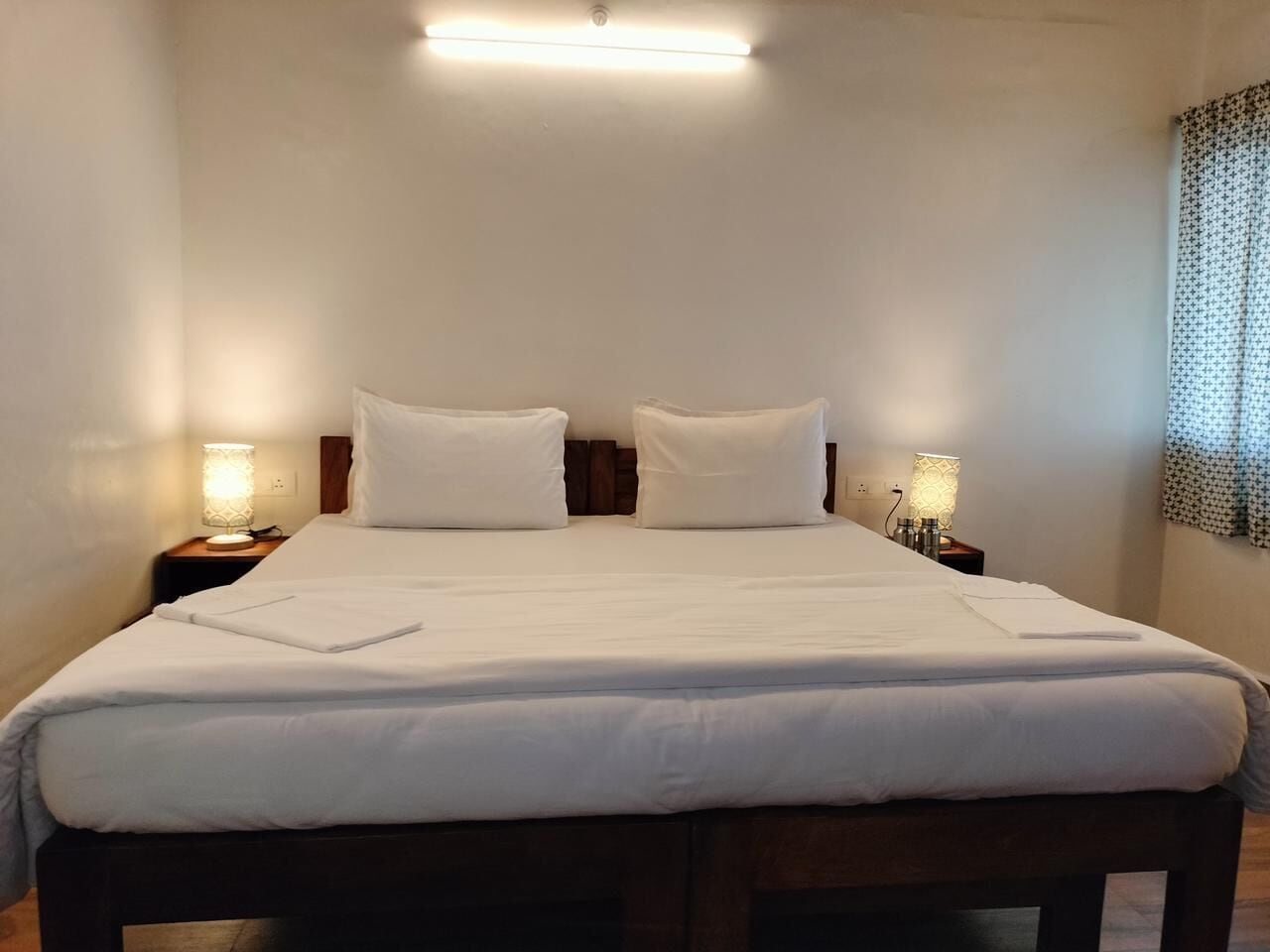 Una cama bien hecha con sábanas blancas, dos lámparas de noche y un cabecero de madera.